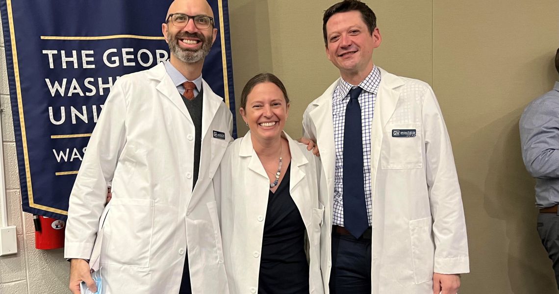 Faculty members Cole, Dring, Wentzell in white coats in front of SMHS banner