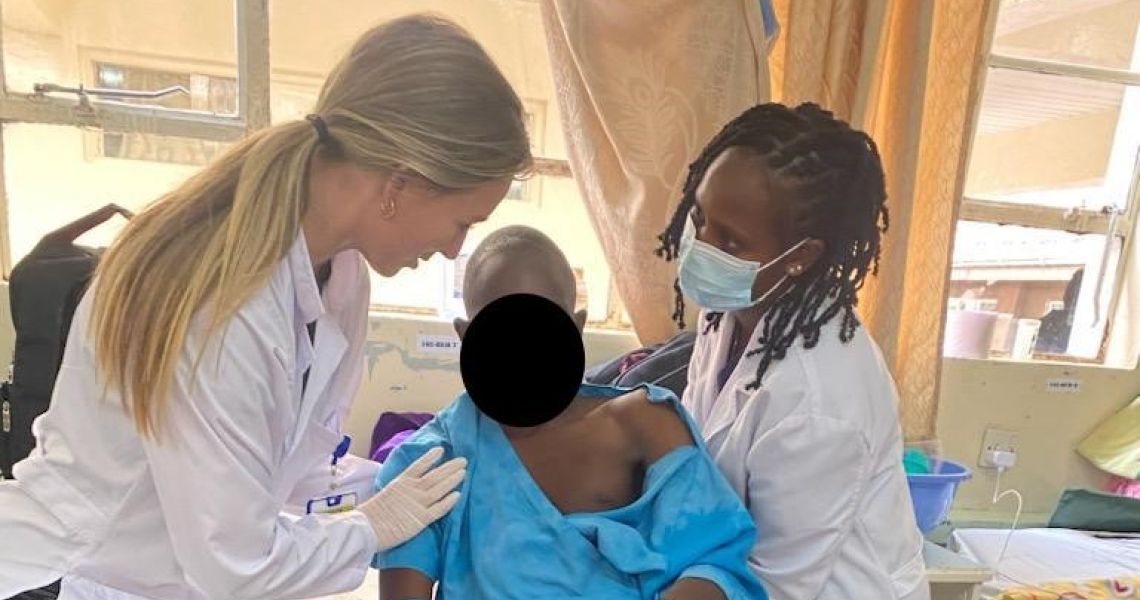 Two female physical therapists help patient to sit up in bed