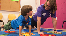 Child and physical therapist doing a push up together in a PT clinic
