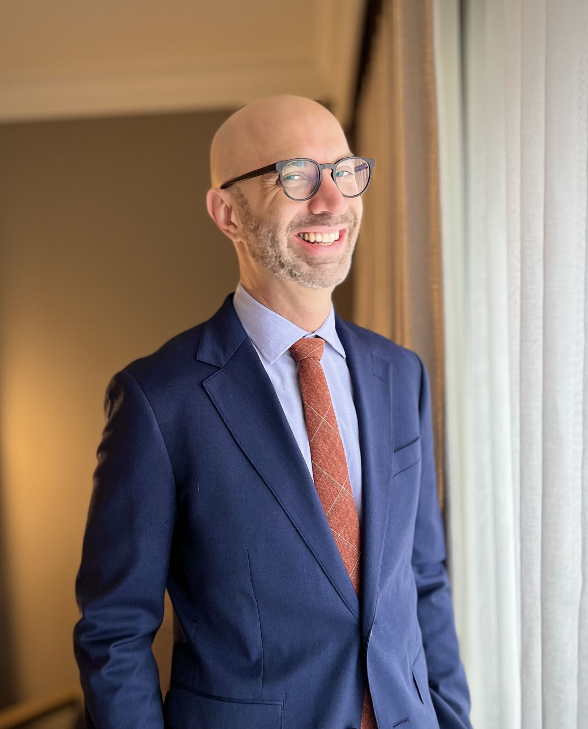 White Male with glasses and suit, standing and smiling