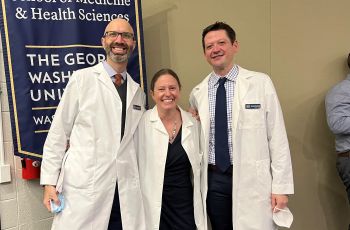 Faculty members Cole, Dring, Wentzell in white coats in front of SMHS banner
