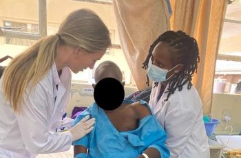 Two female physical therapists help patient to sit up in bed