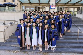 Class of 2025 dressed in graduation robes on steps of library